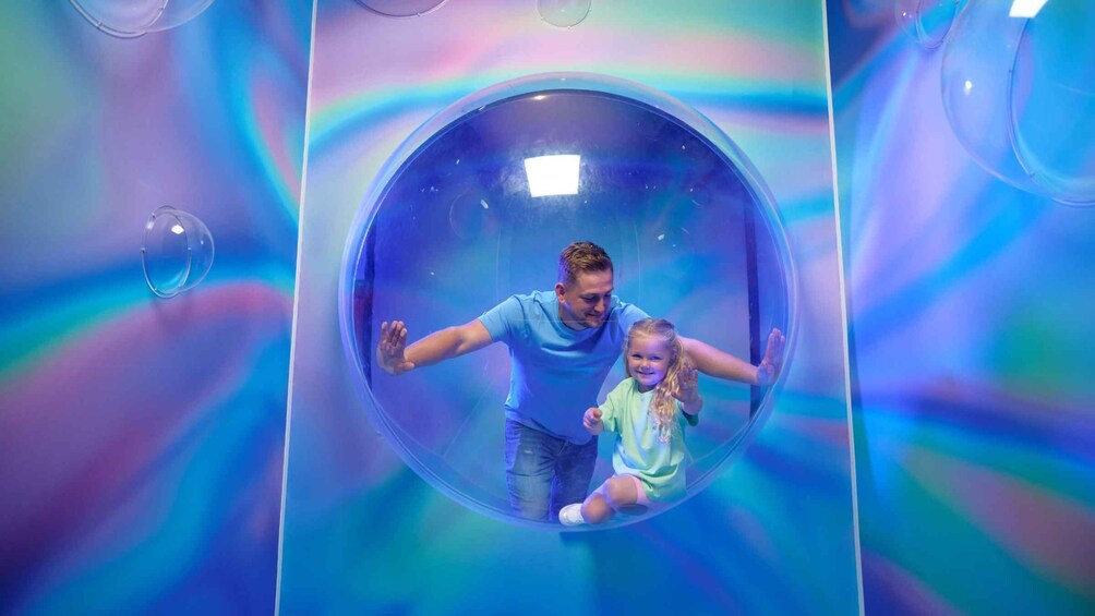 A man and a child inside a transparent spherical structure with a colorful background. 2