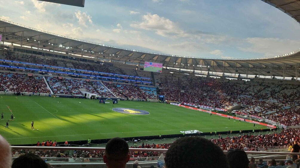 A stadium filled with spectators, a soccer field, and a large digital scoreboard. 1
