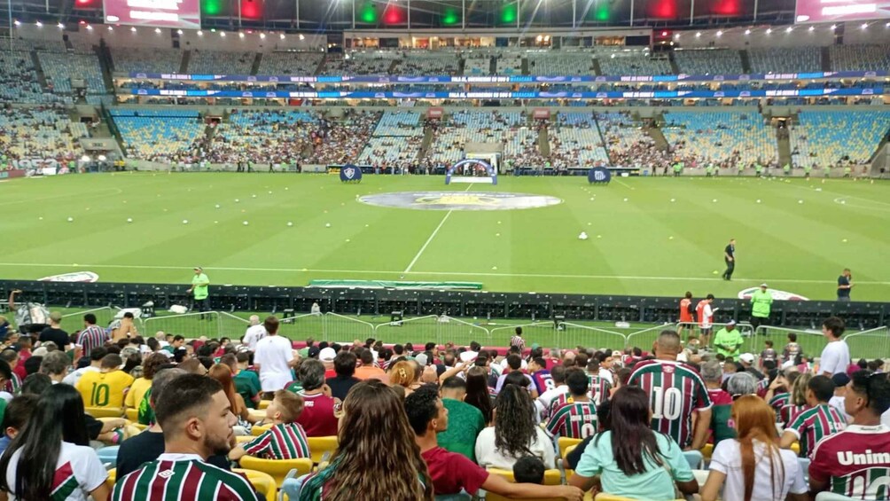 A stadium filled with spectators, a soccer field, and a large digital scoreboard. 3