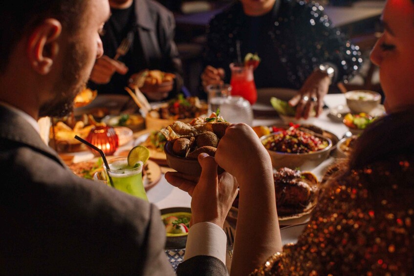 A person holding a bowl of food at a dining table with various dishes and drinks. 3