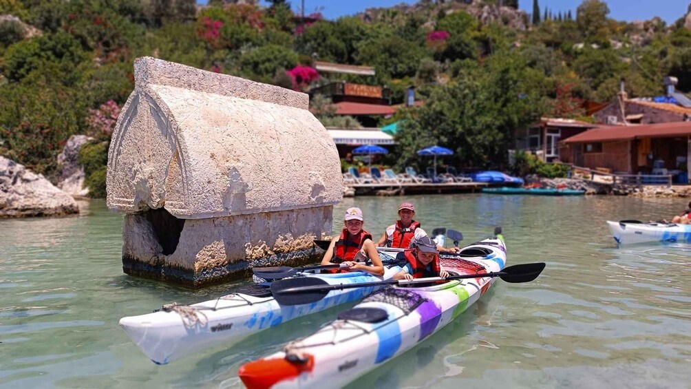 A group of people kayaking on a calm body of water with a stone structure resembling a house in the background. 1