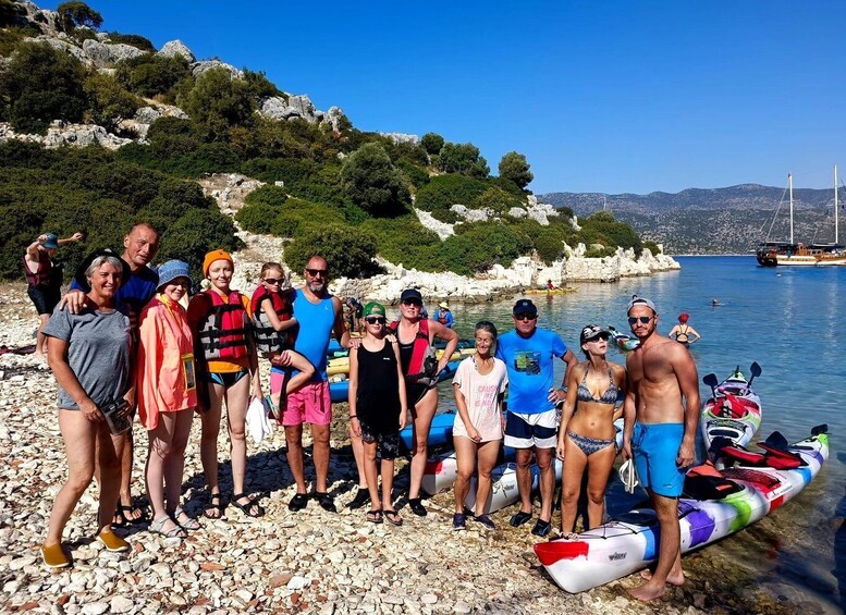 A group of people on a rocky beach with kayaks and a clear blue sky. 2