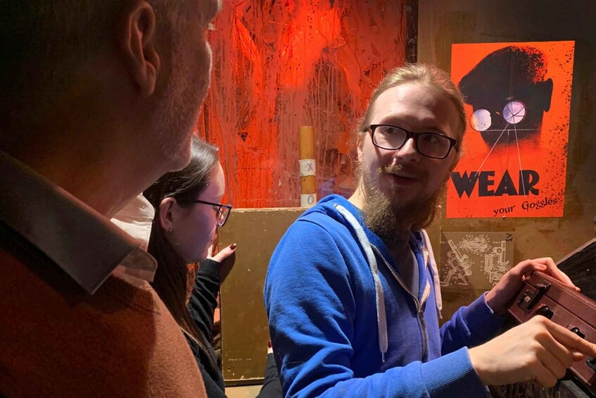 A person holding a device with a red background and a poster with a black silhouette and the text 'WEAR your Goggles'. 4