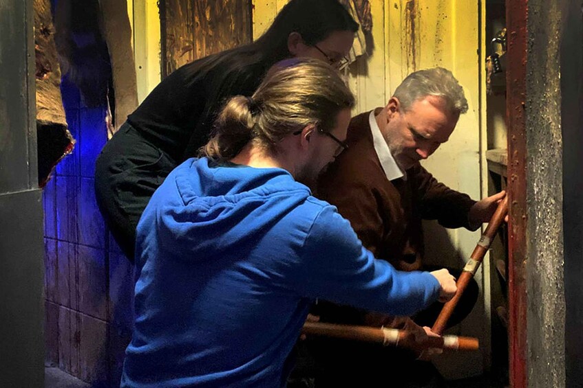 Three people in a dimly lit room, one using a tool on a wooden door. 5