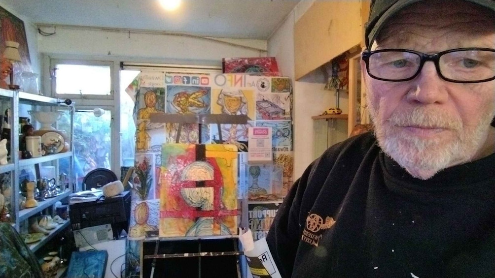 A person in a cluttered room with various items and artwork on the walls. 2