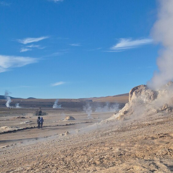 A geothermal area with steam vents, a rocky terrain, and a clear blue sky. 4
