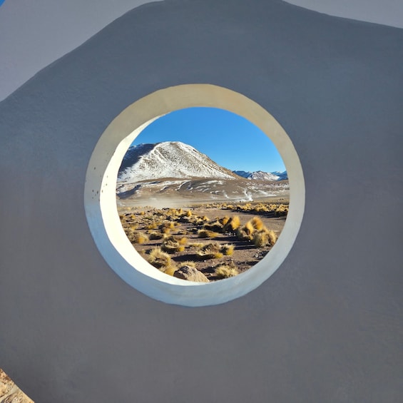 A circular window with a view of a snow-capped mountain and a barren landscape. 1