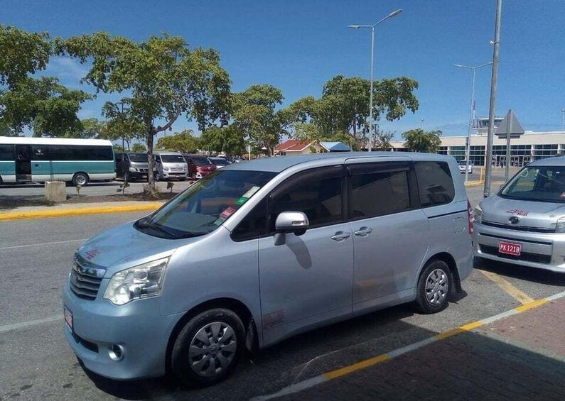 A silver minivan parked in a lot with trees and a building in the background. 5
