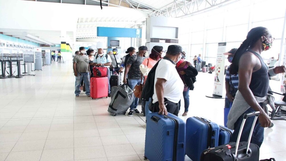 A spacious airport terminal with travelers standing in line, some with luggage. 4