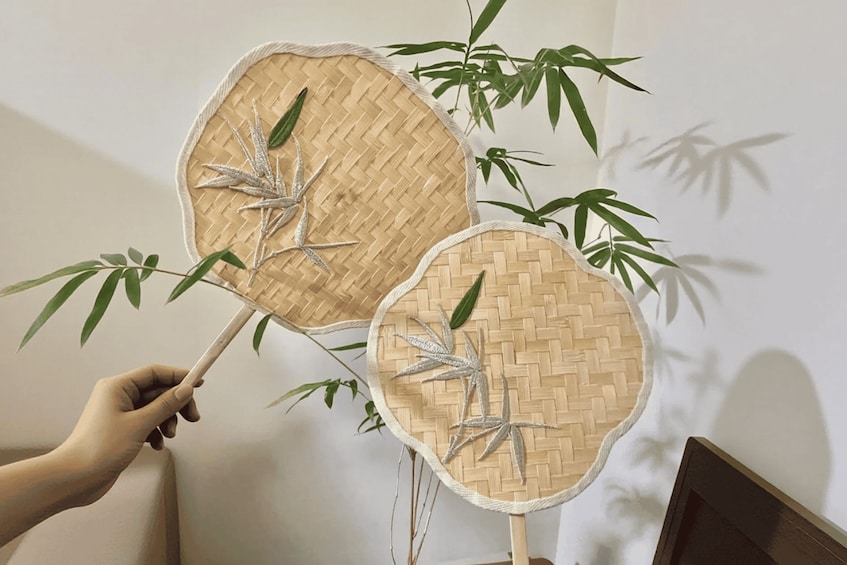 Two woven fans with bamboo leaves, held by a hand. 5
