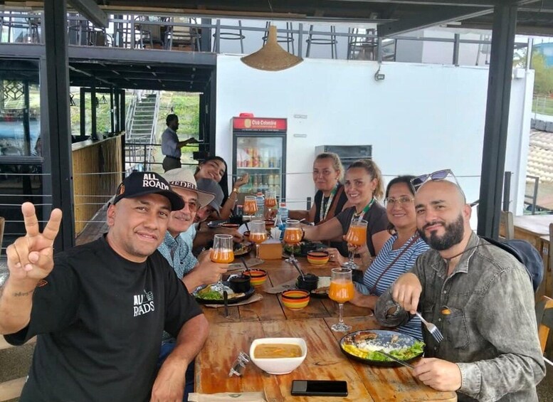 A group of people sitting at a wooden table outdoors, enjoying a meal and drinks. 3