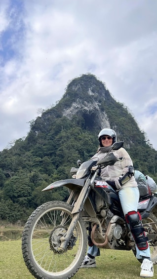 A person on a dirt bike with a helmet, wearing protective gear, and a jacket, standing in front of a mountain. 2