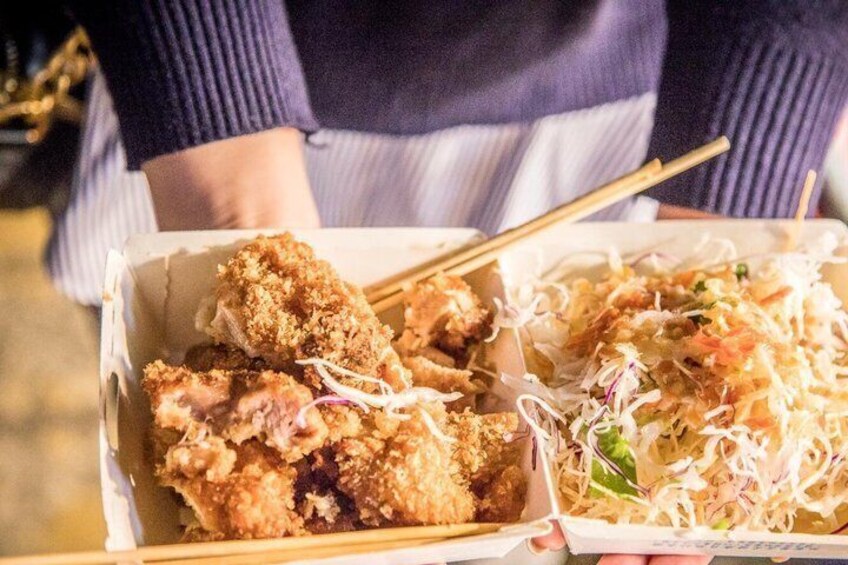 A person holding a box of fried chicken and a side of shredded cabbage. 4