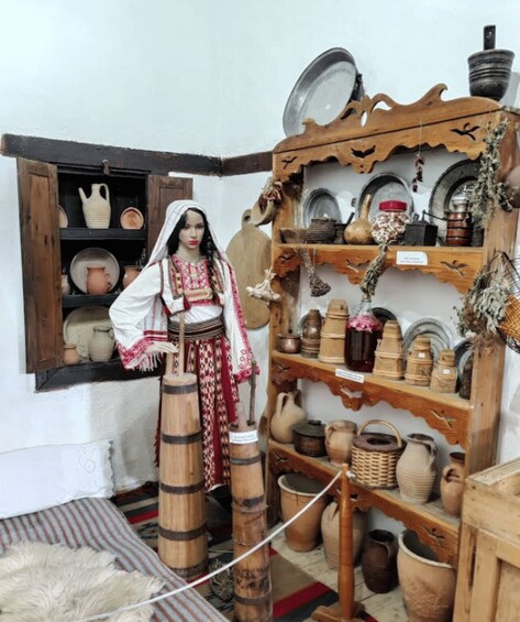 A mannequin in traditional attire, wooden barrels, and a variety of pottery and ceramics on shelves. 1