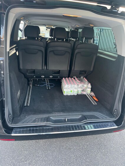 The interior of a vehicle with three black seats, a rearview mirror, and a storage area containing bottled water and a cleaning tool. 2
