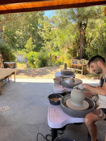 A person engaged in pottery making outdoors, surrounded by trees and a wooden structure. 4