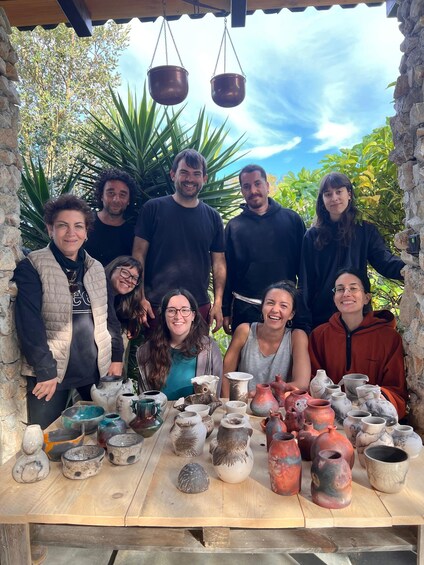 A group of people gathered around a table with various pottery items. 5