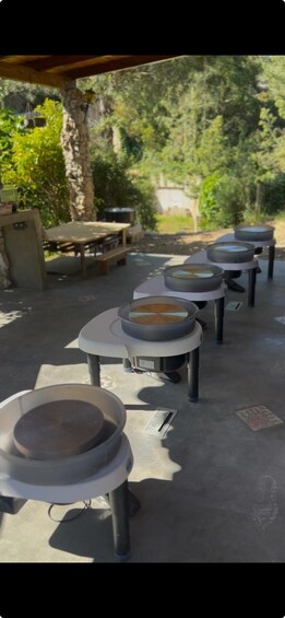 Outdoor tables with round tops, likely for dining or serving, under a covered area with trees in the background. 3