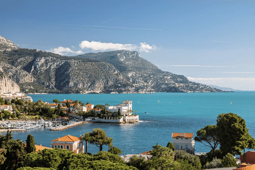 A coastal town with buildings, a marina, and a mountainous backdrop. 2