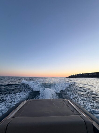 A boat's wake in the ocean with a clear sky and a coastline in the distance. 1