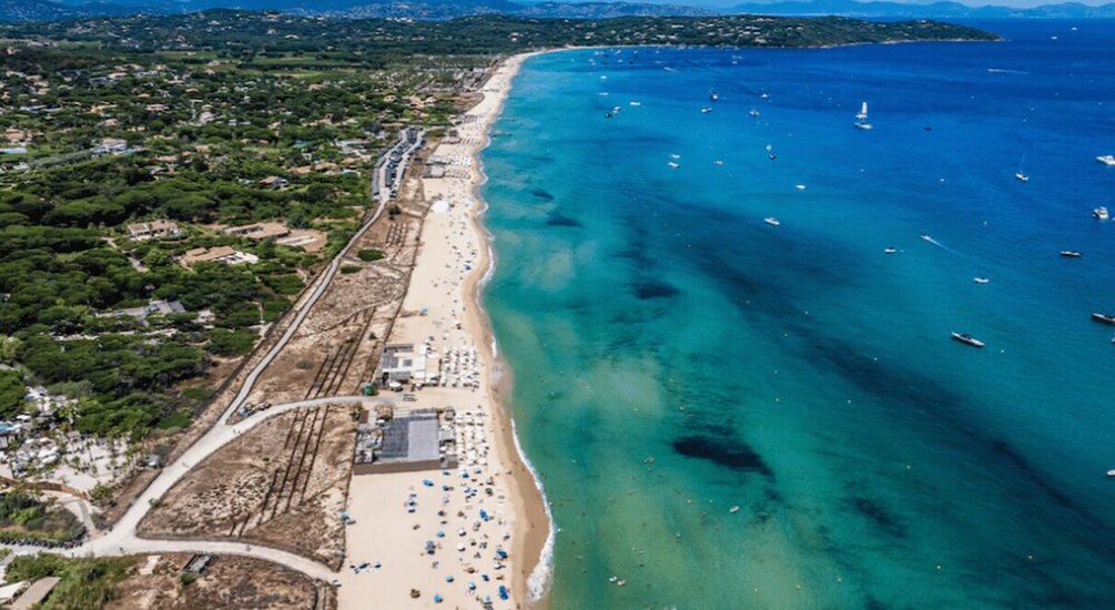 An aerial view of a coastal area with a sandy beach, a road, and a clear blue sea with boats. 5