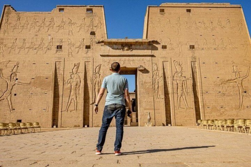 A man standing in front of an ancient Egyptian temple with hieroglyphics and statues. 2