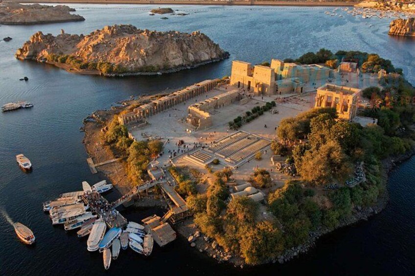 An ancient fortified island with ruins, boats docked at the shore, and a large rock formation in the background. 4