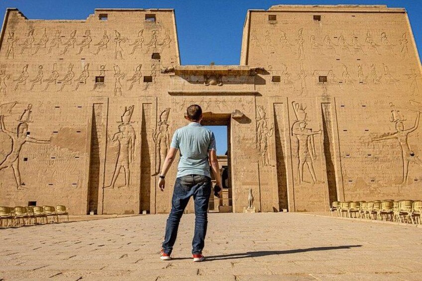A person standing in front of a large ancient Egyptian temple with hieroglyphics. 2