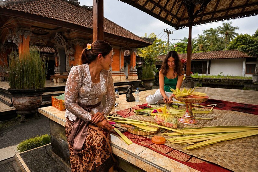 Two women engaged in a traditional activity with ritual items and a decorated mat outdoors. 1