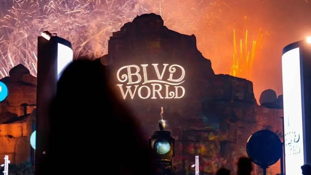 A silhouette of a person in front of a sign that reads 'BLVD WORLD' with a backdrop of a rocky structure and fireworks. 1