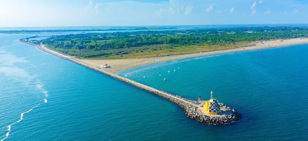 An aerial view of a coastal area with a long pier extending into the water, a sandy beach, and a green landscape in the background. 5