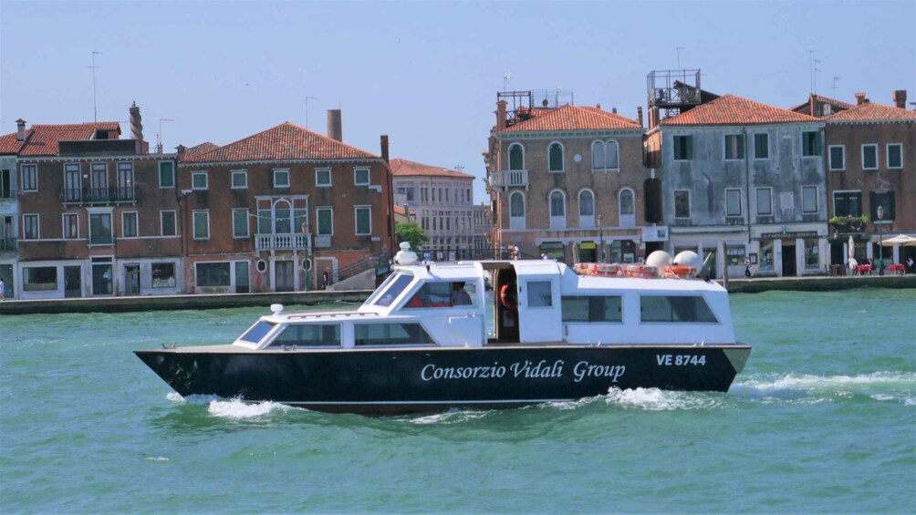 A boat named Consorzio Vidali Group moving through a canal with buildings in the background. 2
