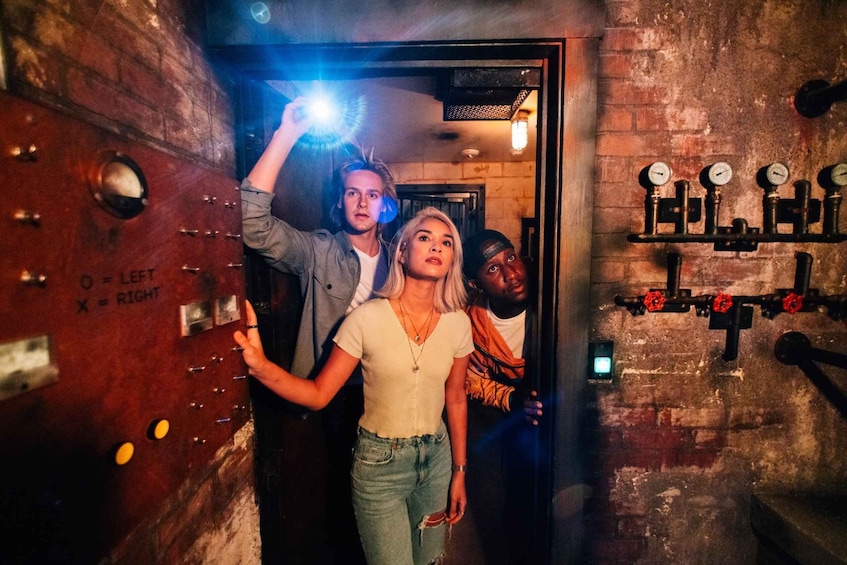 A group of people in a dimly lit room with industrial elements like pipes and gauges. 2