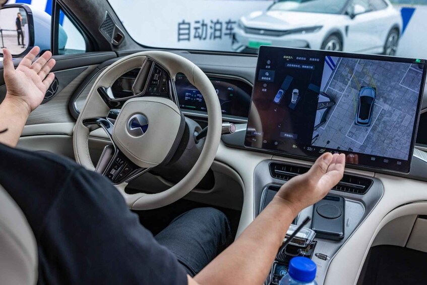 A person driving a self-driving car with a digital display showing a map and vehicle controls. 1
