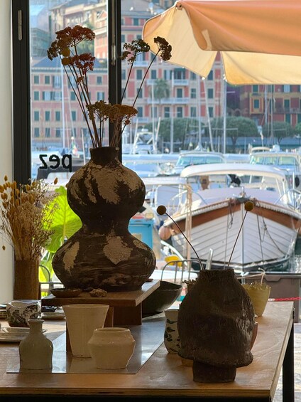 A rustic vase with dried flowers on a table, a cityscape with boats in the background, and a window with a view of buildings. 3
