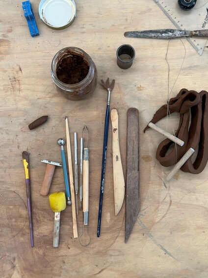 A variety of tools and materials laid out on a wooden surface, including paintbrushes, a jar of paint, a ruler, and a pair of scissors. 5