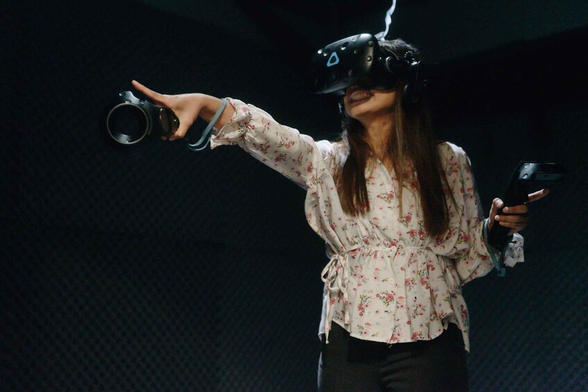 A person wearing a VR headset, holding a VR controller in one hand and a cup in the other. 3