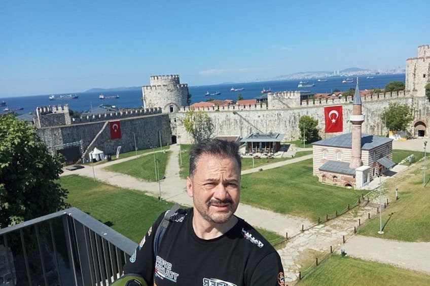 A man standing on a balcony overlooking a historic fort with a view of the sea and a flag. 1