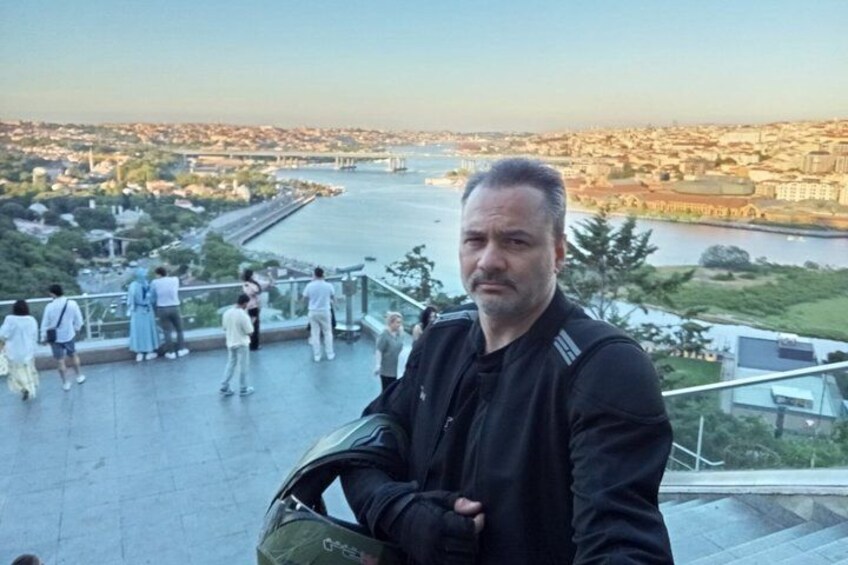 A man standing on a viewing platform overlooking a river with a cityscape in the background. 4