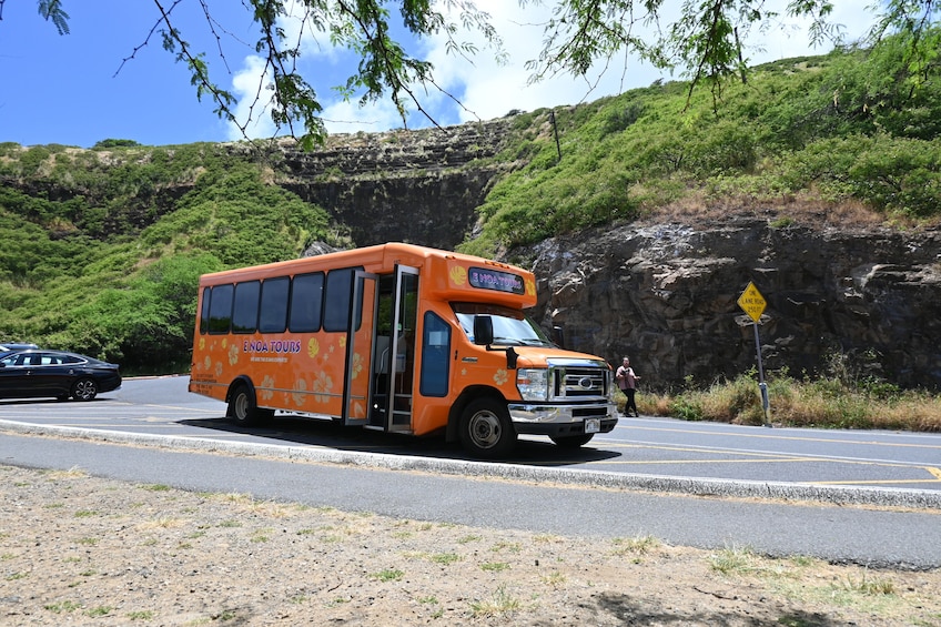 A bus with 'ENOA TOURS' written on the side driving on a road with a rocky cliff in the background. 5