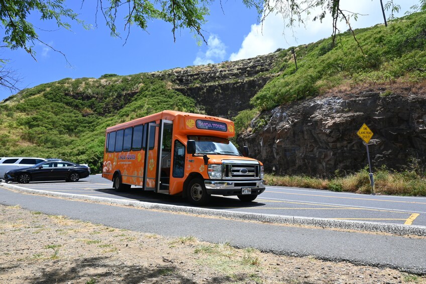 An orange tour bus on a road with a rocky hill in the background. 4