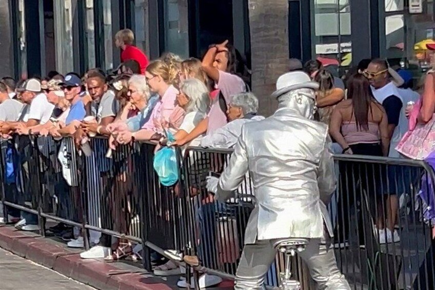 A crowd of people gathered around a performer in a shiny silver costume. 3