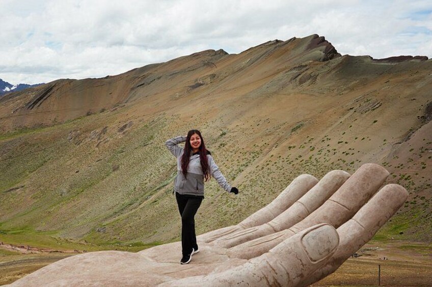 A person standing on a large hand sculpture in a mountainous landscape. 2