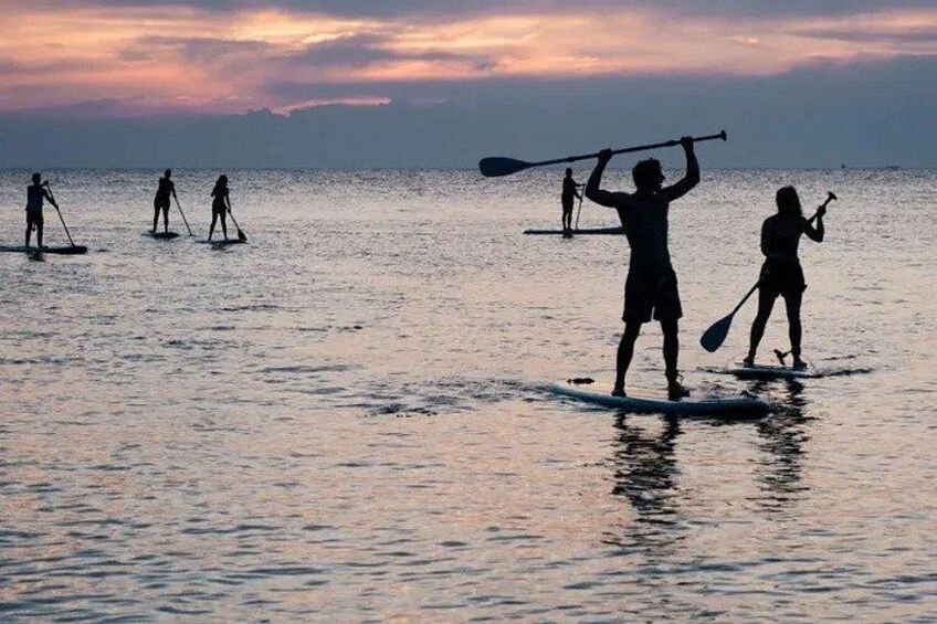 People paddleboarding on a calm sea during sunset. 4