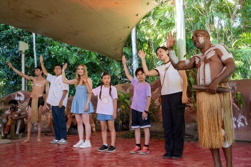 A group of people in a tropical setting with a covered area and lush greenery in the background. 1