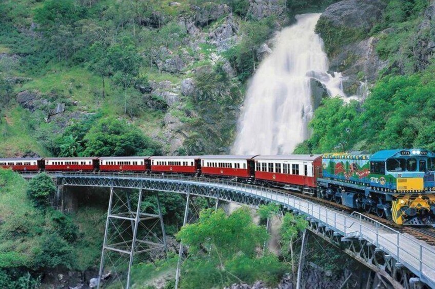 A train on a bridge over a waterfall in a forested area. 3