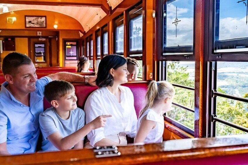 A family on a train with large windows, a wooden interior, and a view of the landscape outside. 4