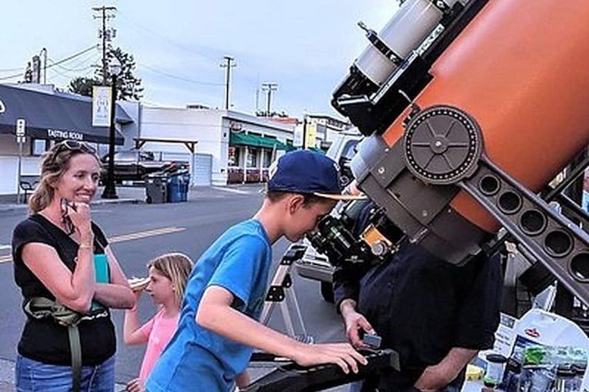 A person operating a large orange telescope, with a woman and a child observing. 2