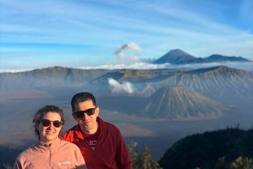Two people standing with a mountainous landscape in the background. 1