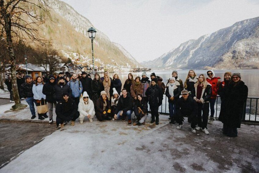 A group of people posing by a lake with snow-covered mountains in the background. 1